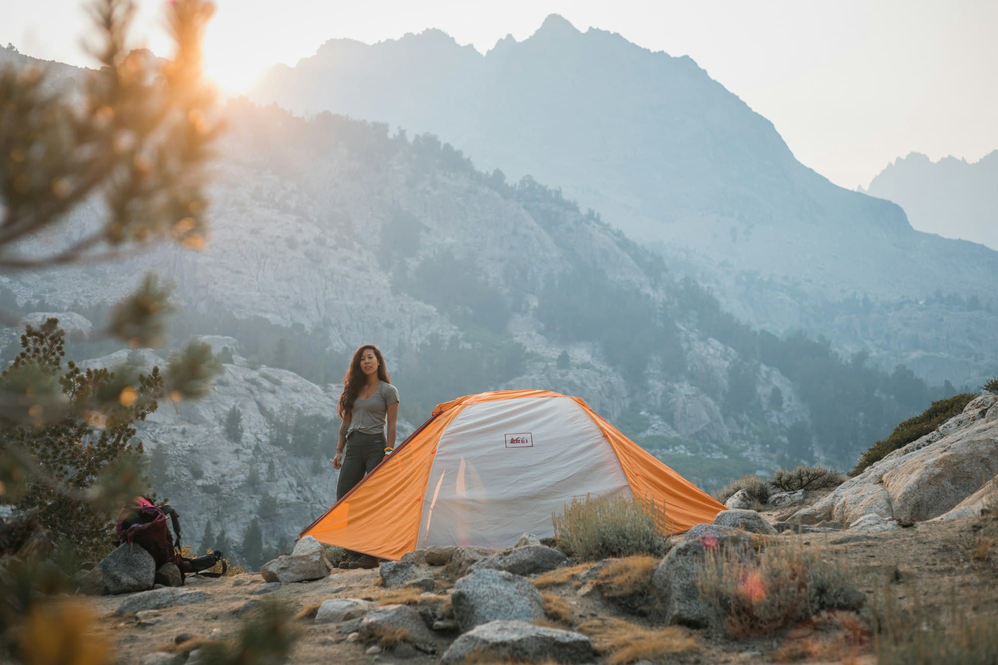 Camper standing beside an orange tent on a rocky mountainside