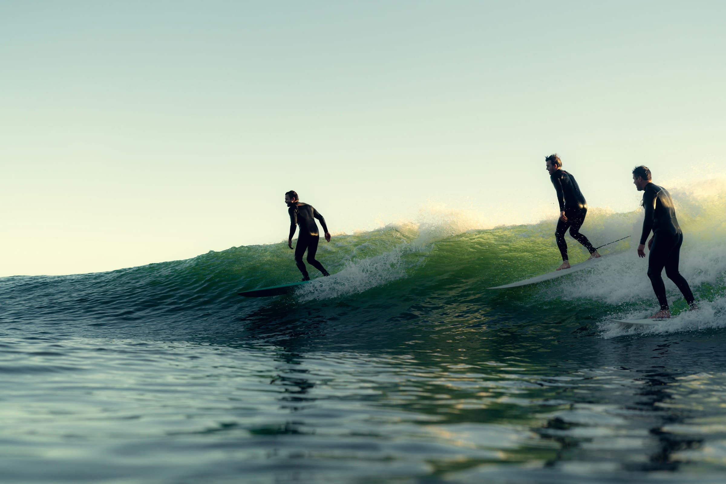 Three surfers riding a glassy wave together at golden hour